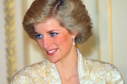 Princess Diana wearing white suit and pearl earrings, smiling warmly at a royal event.