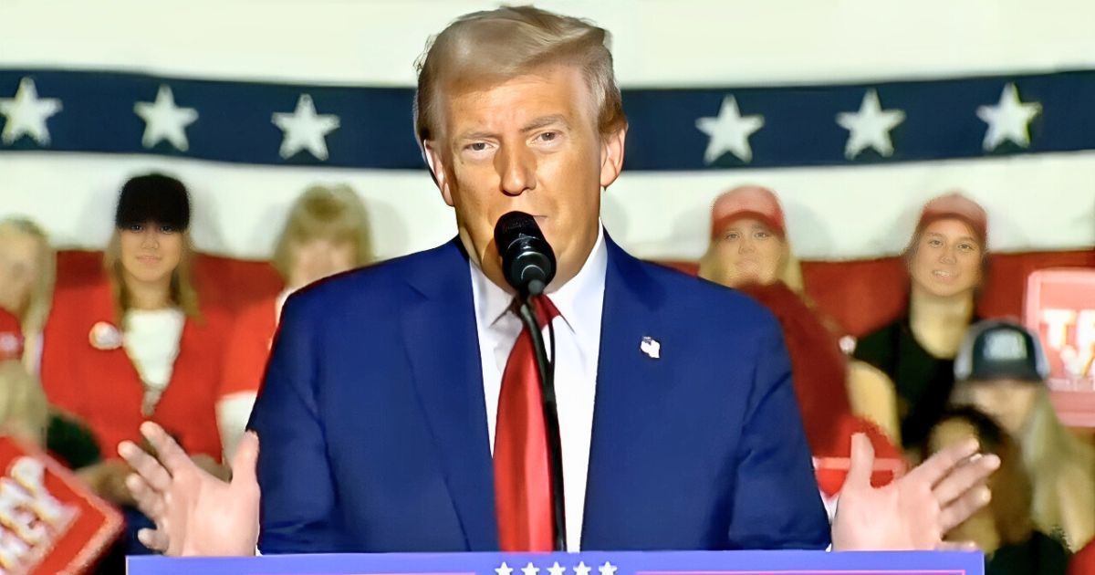 President Donald Trump speaking at a podium with U.S. flags in the background, mid-speech